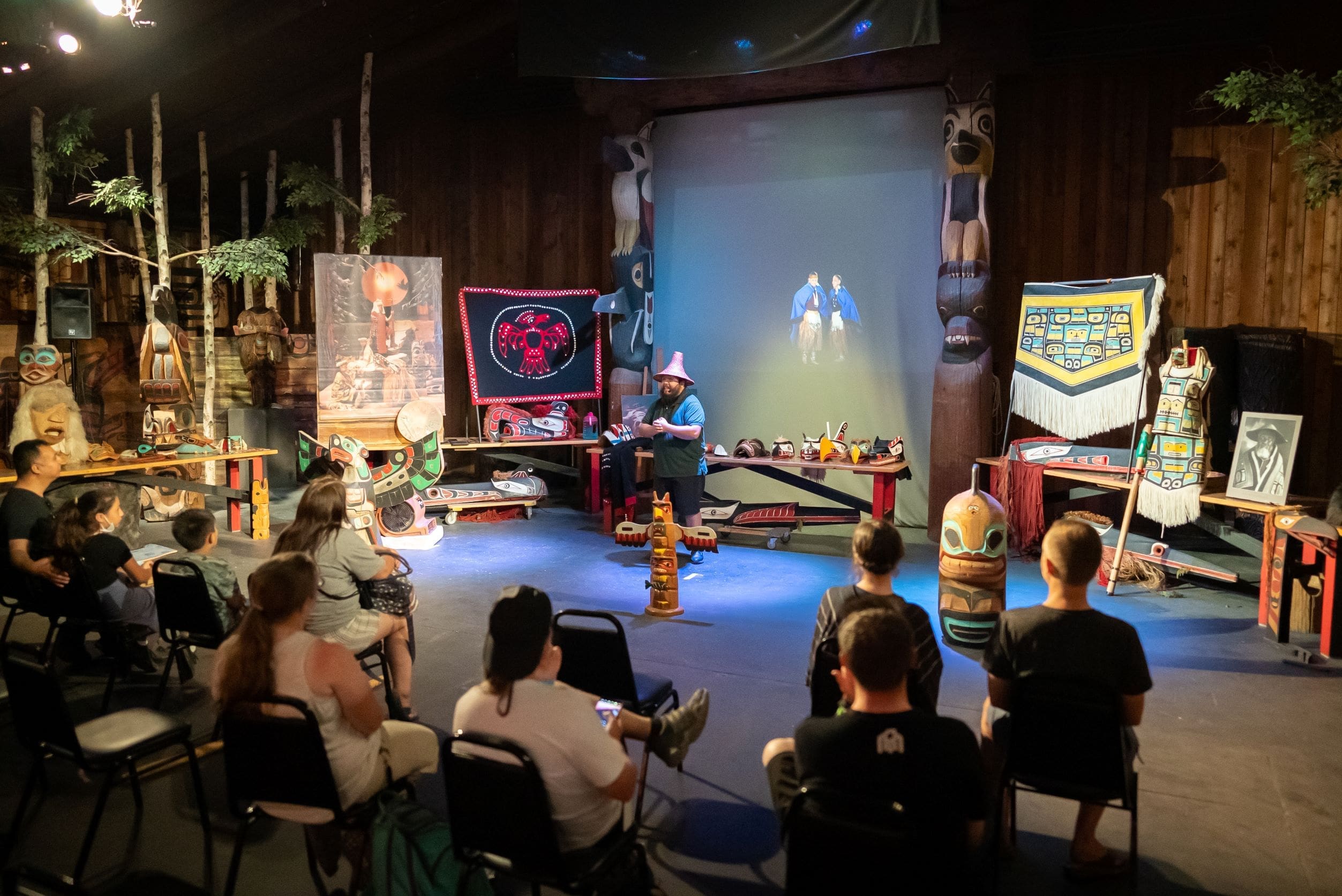 People in theater watching presenter, surrounded by Native American regalia